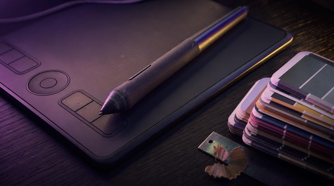 Graphics tablet and stylus beside colour swatch cards, representing precise twitch emote size design work.
